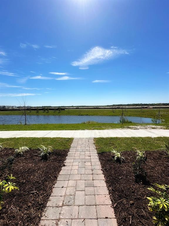 A stone walkway leads toward a pond and a grassy field under a clear blue sky — 2639 CANDIED APPLE ALLEY, KISSIMMEE, FL