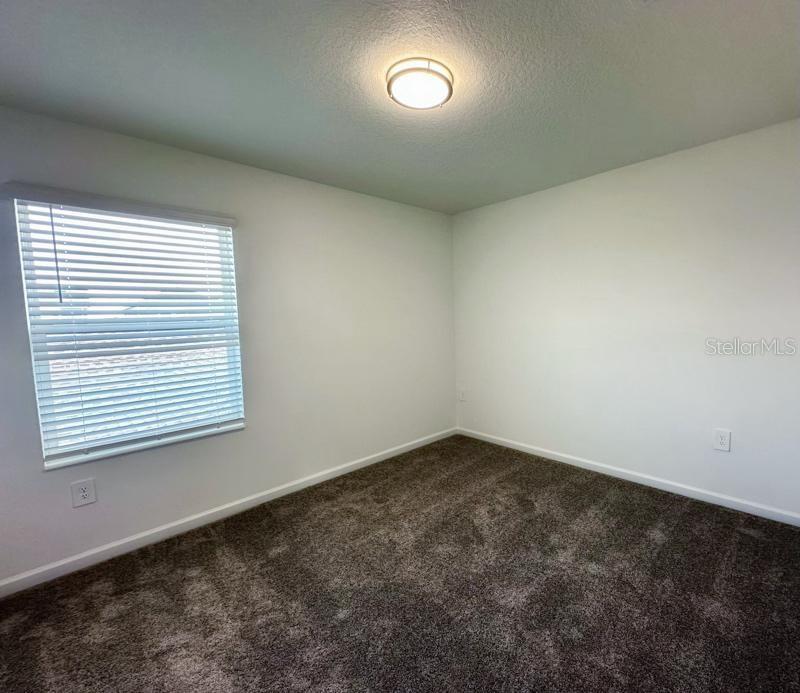 An empty bedroom features white walls, dark gray carpeting, a window with blinds, and a ceiling light — 2639 CANDIED APPLE ALLEY, KISSIMMEE, FL