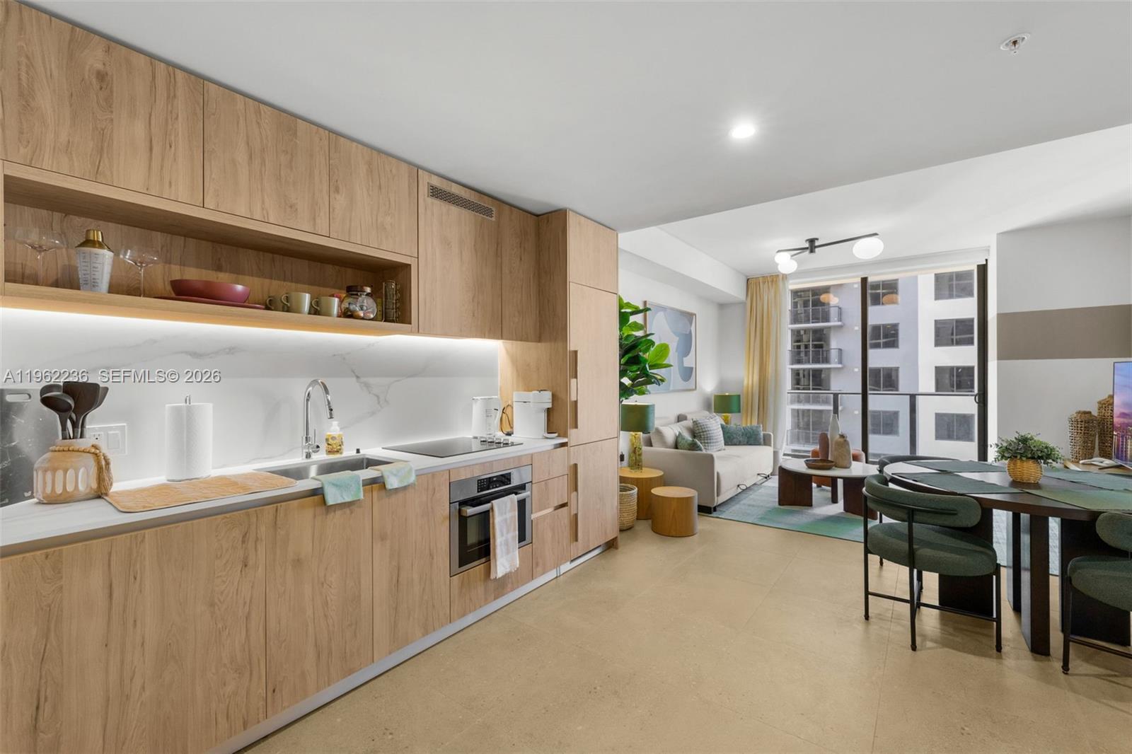 A modern kitchen with light wood cabinetry and marble backsplash opens into a living area — 11 NE 6th St # 1611, Miami FL 33132, MIAMI, FL