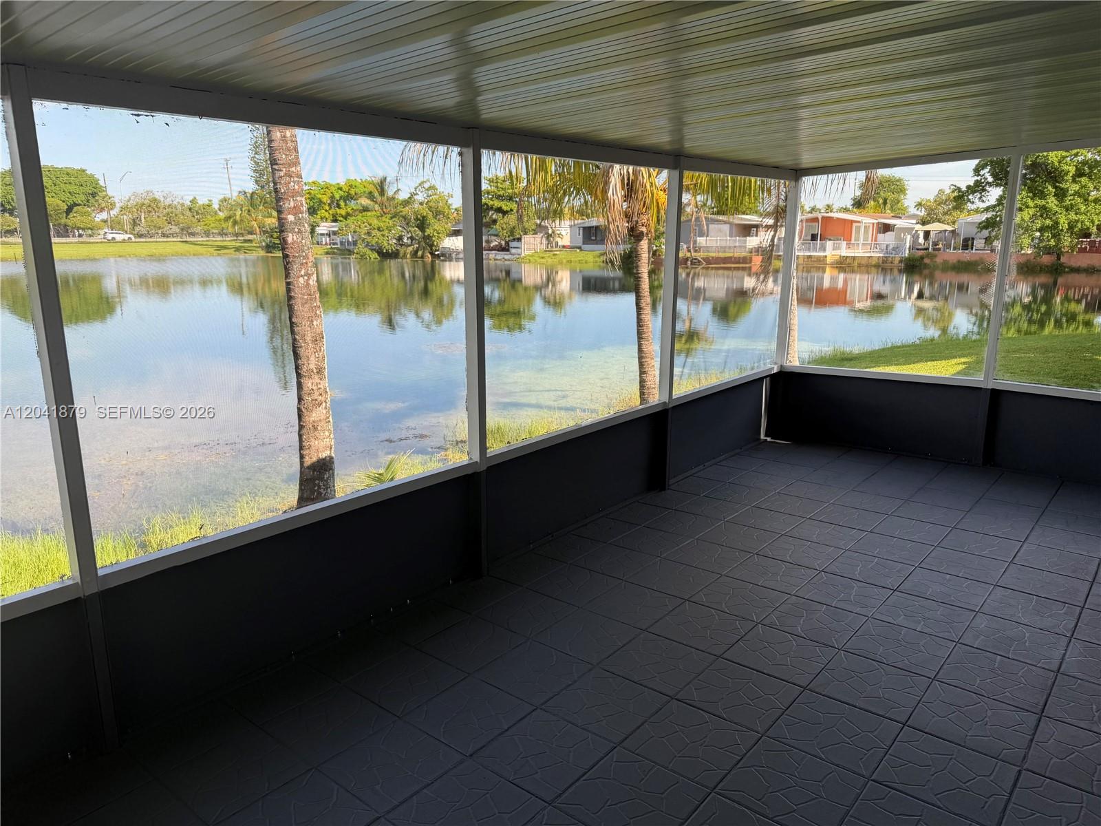 A screened-in porch with dark tiled flooring overlooks a lake and palm trees — 20606 NW 55th Court # A, Opa-Locka FL 33055, OPA-LOCKA, FL