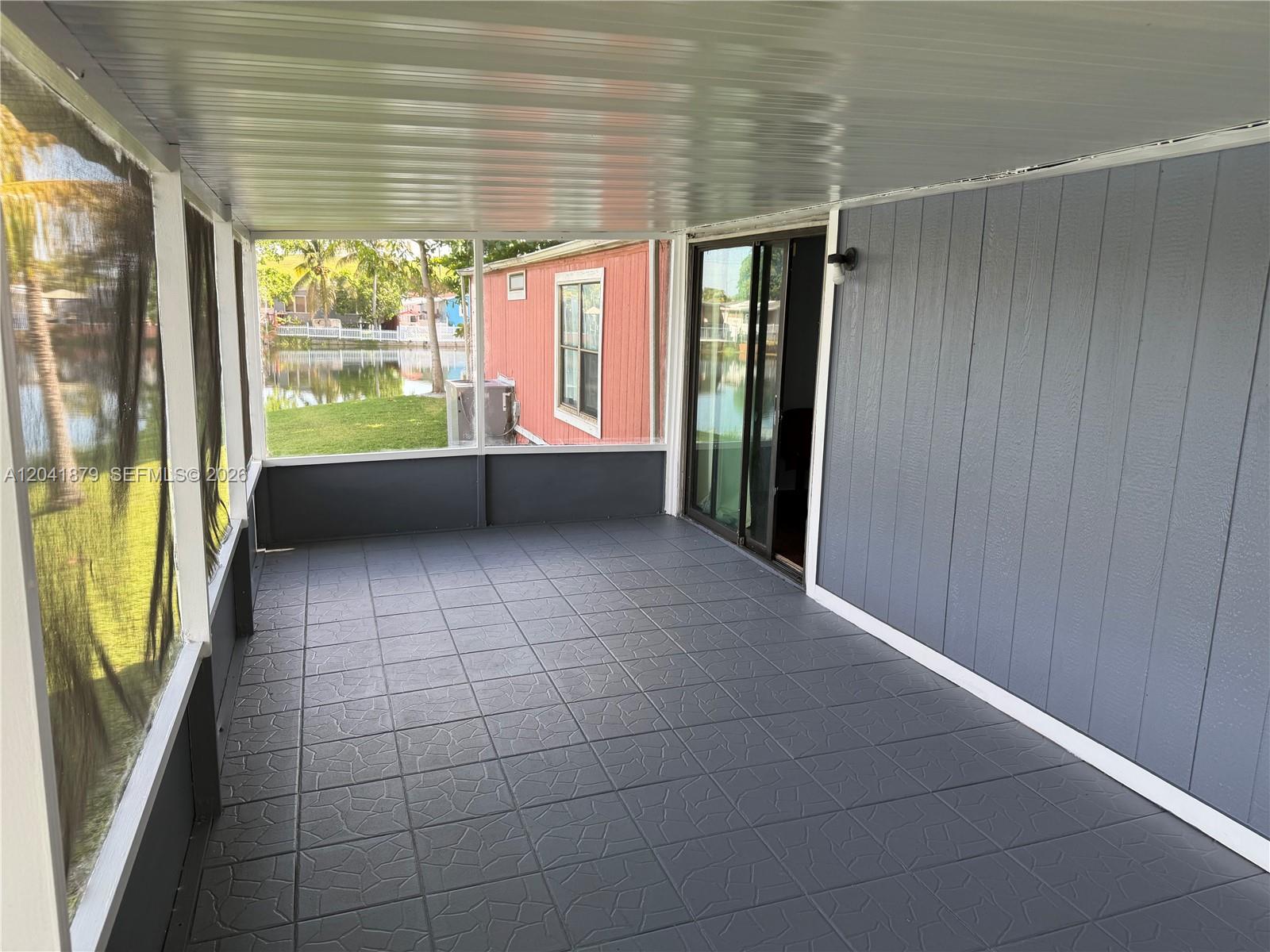 A screened-in porch features gray tiled flooring, a sliding glass door, and a water view — 20606 NW 55th Court # A, Opa-Locka FL 33055, OPA-LOCKA, FL