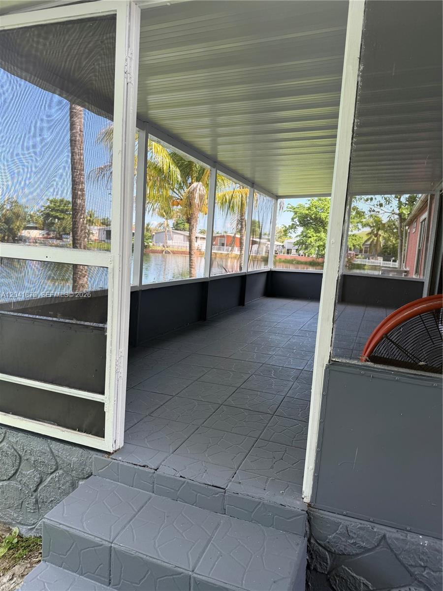 A screened-in porch features gray tiled flooring and a view of a nearby lake — 20606 NW 55th Court # A, Opa-Locka FL 33055, OPA-LOCKA, FL