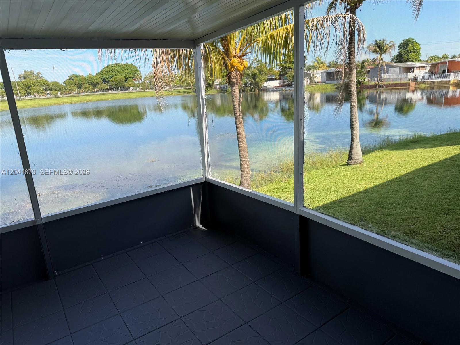 A screened-in patio features dark tiled flooring and a view of a lake and palm trees — 20606 NW 55th Court # A, Opa-Locka FL 33055, OPA-LOCKA, FL