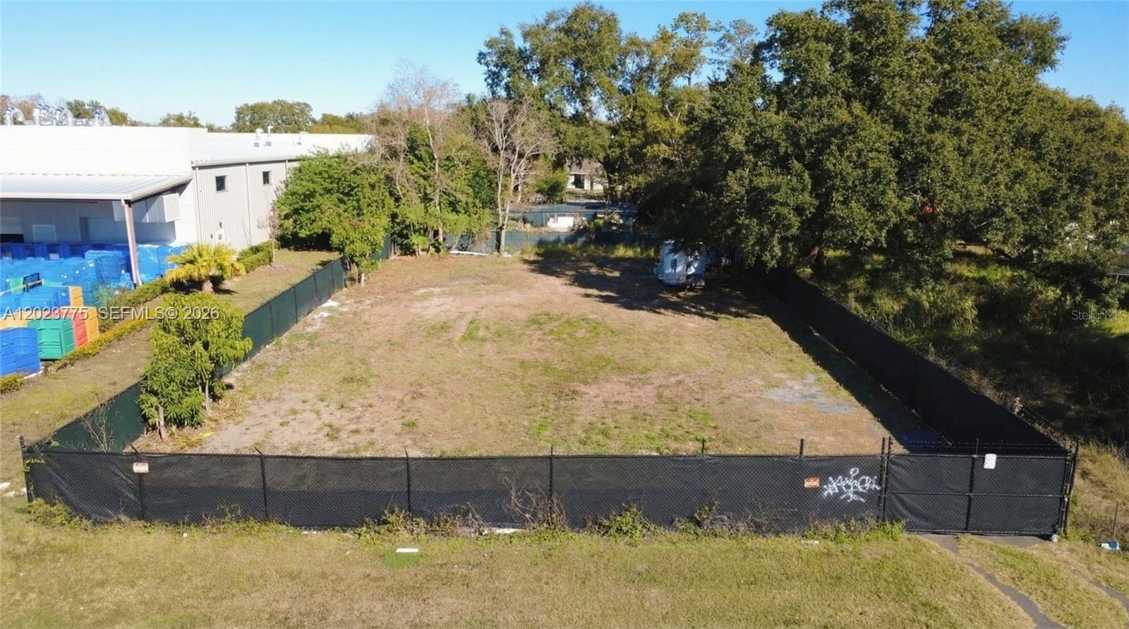An aerial view shows a rectangular, fenced-in vacant lot with sparse grass and surrounding trees — 303 E LANCASTER, Orlando FL 32809, ORLANDO, FL