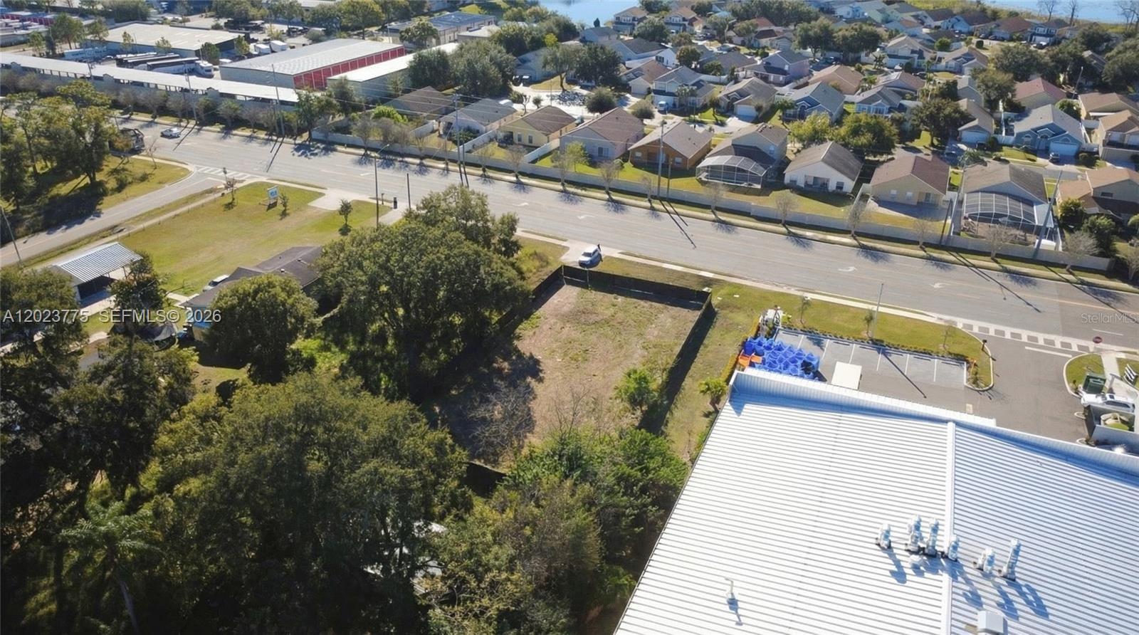 An aerial view shows a vacant rectangular lot situated between a commercial building and trees — 303 E LANCASTER, Orlando FL 32809, ORLANDO, FL