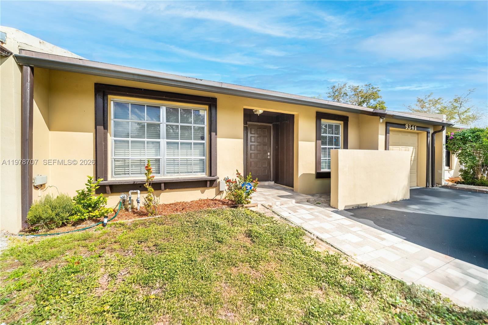 A single-story house exterior features a yellow facade, dark trim, and a paved walkway — 9341 E Fern Ln, Miramar FL 33025, MIRAMAR, FL