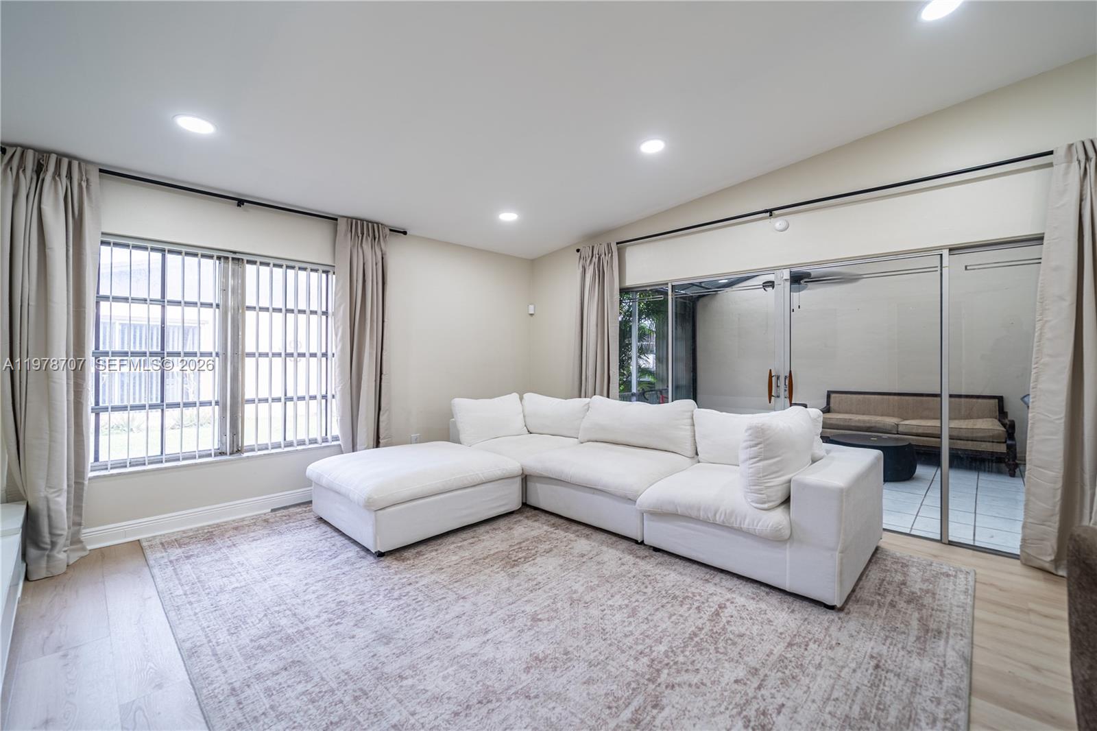 A living room features a white sectional sofa, a patterned area rug, and sliding glass doors — 9341 E Fern Ln, Miramar FL 33025, MIRAMAR, FL
