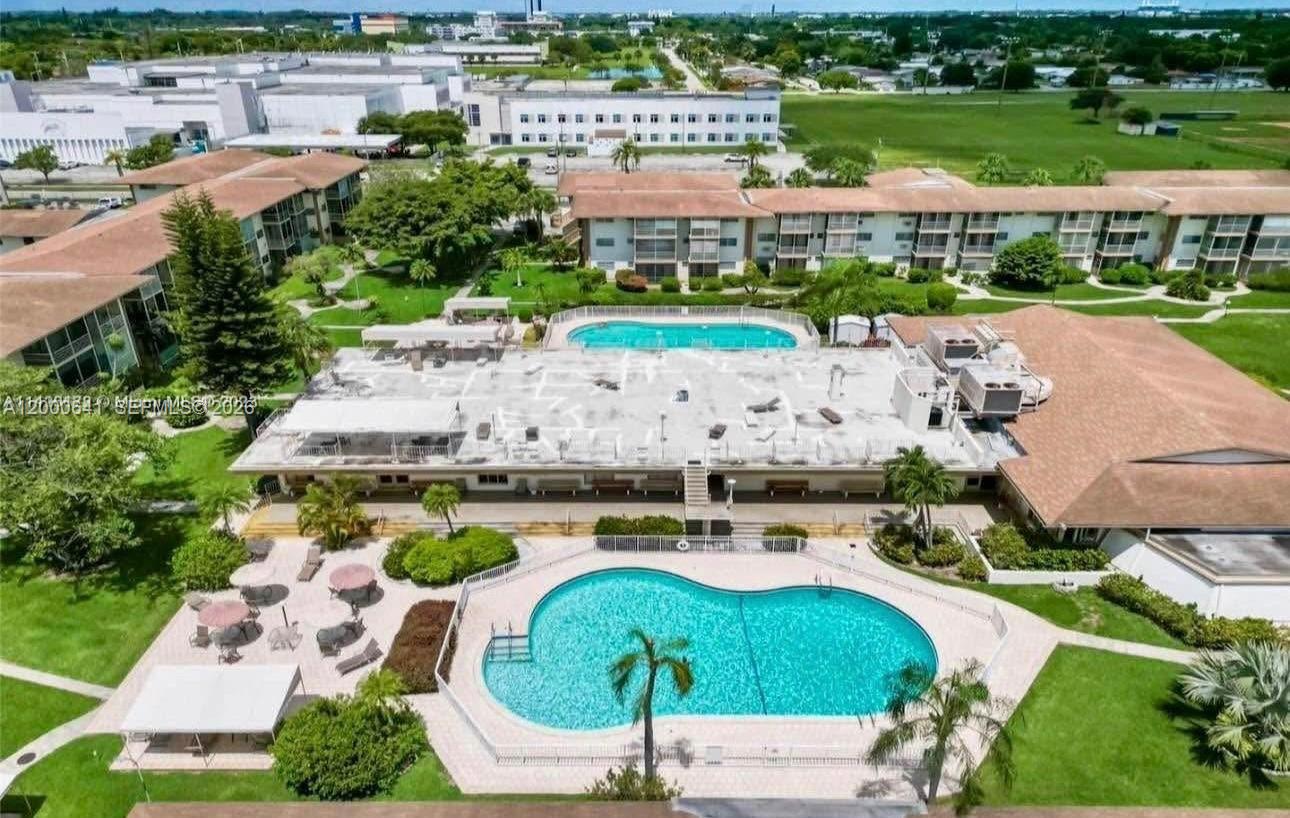 An aerial view shows a community clubhouse with two swimming pools and surrounding apartment buildings — 16900 NE 14 # 109, Miami FL 33162, MIAMI, FL