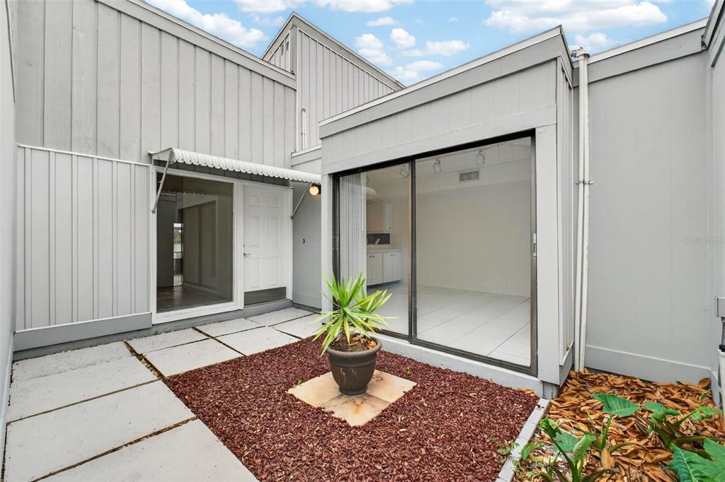 A gray-sided building features a small courtyard with concrete pavers, red mulch, and sliding doors — 1502 BUCKEYE ROAD NE UNIT 4, WINTER HAVEN, FL