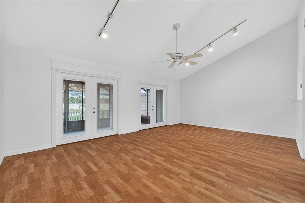 An empty room with wood-look flooring, white walls, a vaulted ceiling, and two glass doors — 1502 BUCKEYE ROAD NE UNIT 4, WINTER HAVEN, FL