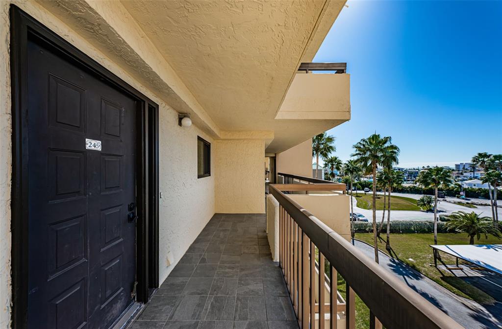 An outdoor balcony with dark tile flooring, a black door, and a metal railing — 401 150TH AVENUE UNIT 245, MADEIRA BEACH, FL