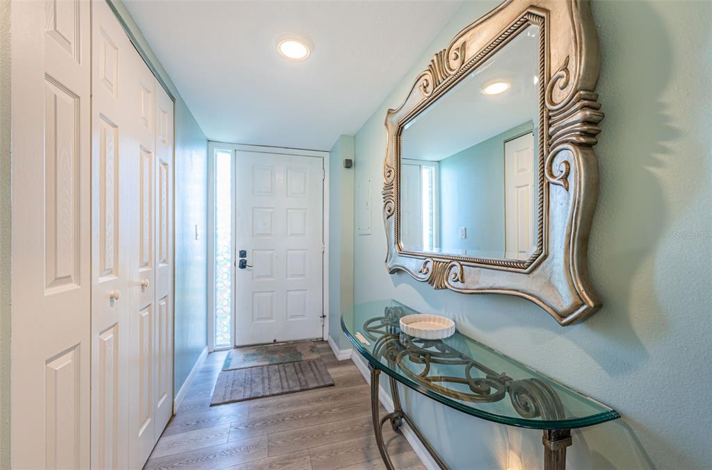 An entryway features light blue walls, wood-look flooring, a glass console table, and a mirror — 401 150TH AVENUE UNIT 245, MADEIRA BEACH, FL