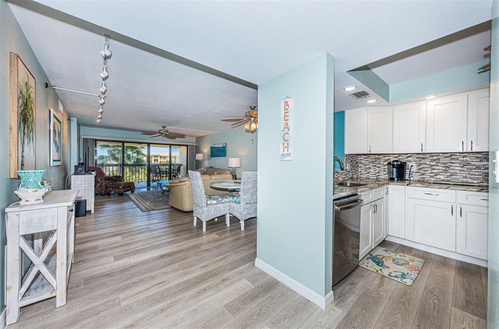 An open-concept living area features light wood flooring, a kitchen with white cabinets, and balcony — 401 150TH AVENUE UNIT 245, MADEIRA BEACH, FL