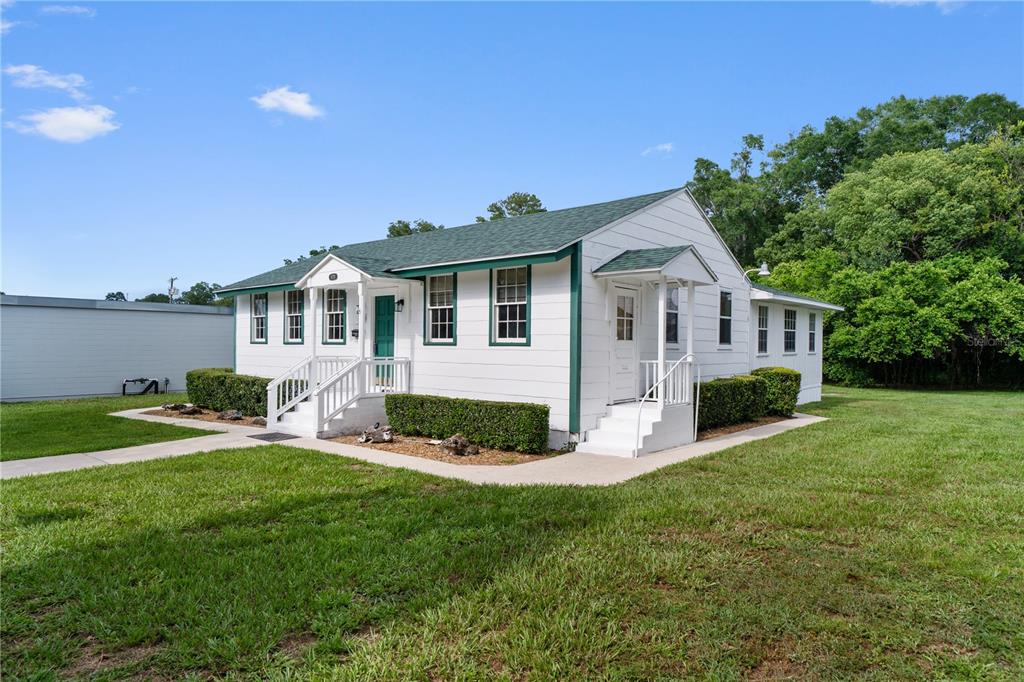 A white, single-story house with a green roof and trim sits on a grassy lot — 14721 MAIN STREET, ALACHUA, FL