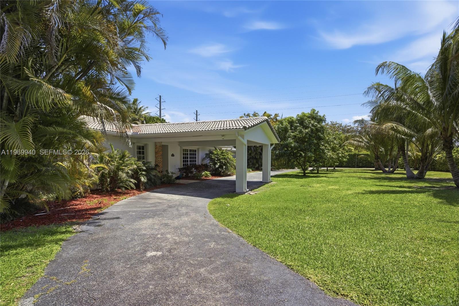 A paved driveway leads to a covered carport attached to a single-story house with palm trees — 14721 SW 67th Ave, Coral Gables FL 33158, CORAL GABLES, FL