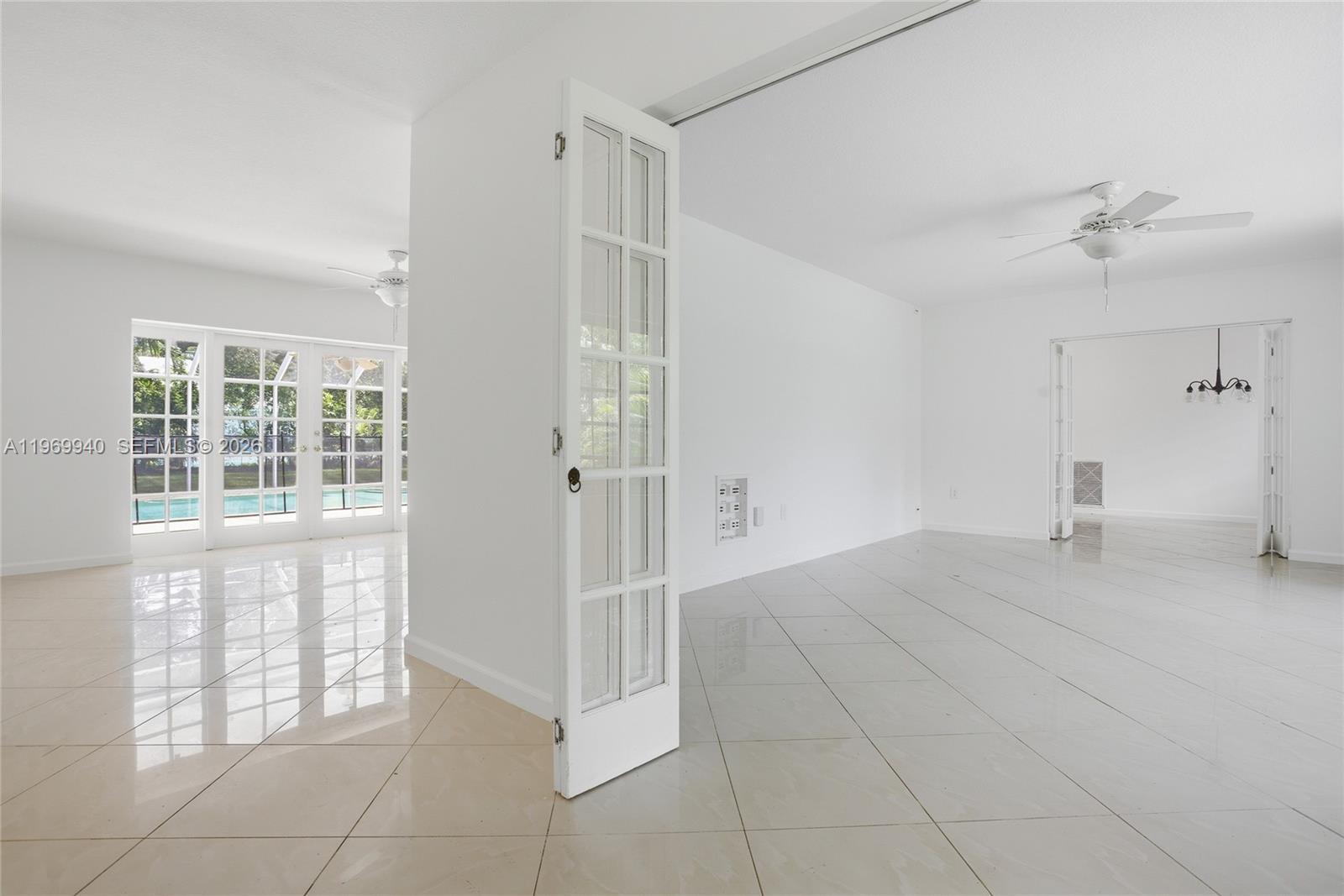 A bright, open-concept room features white walls, tiled floors, French doors, and ceiling fans — 14721 SW 67th Ave, Coral Gables FL 33158, CORAL GABLES, FL