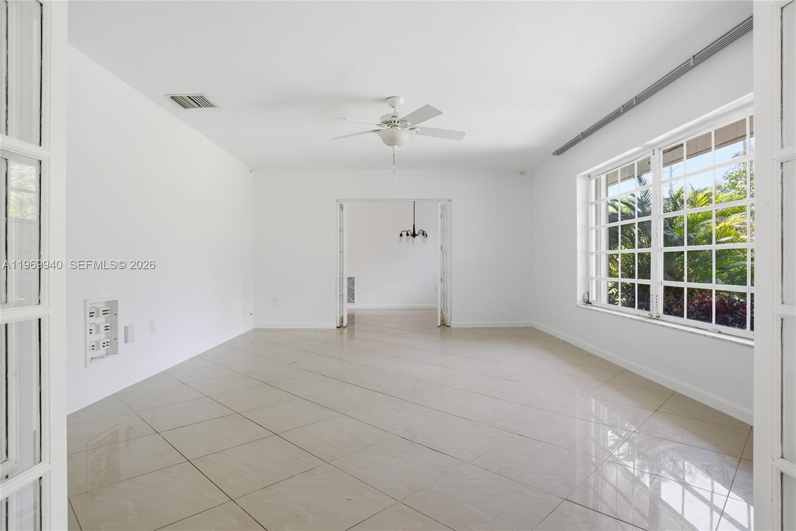 A bright, empty room features white walls, tile flooring, a ceiling fan, and large windows — 14721 SW 67th Ave, Coral Gables FL 33158, CORAL GABLES, FL