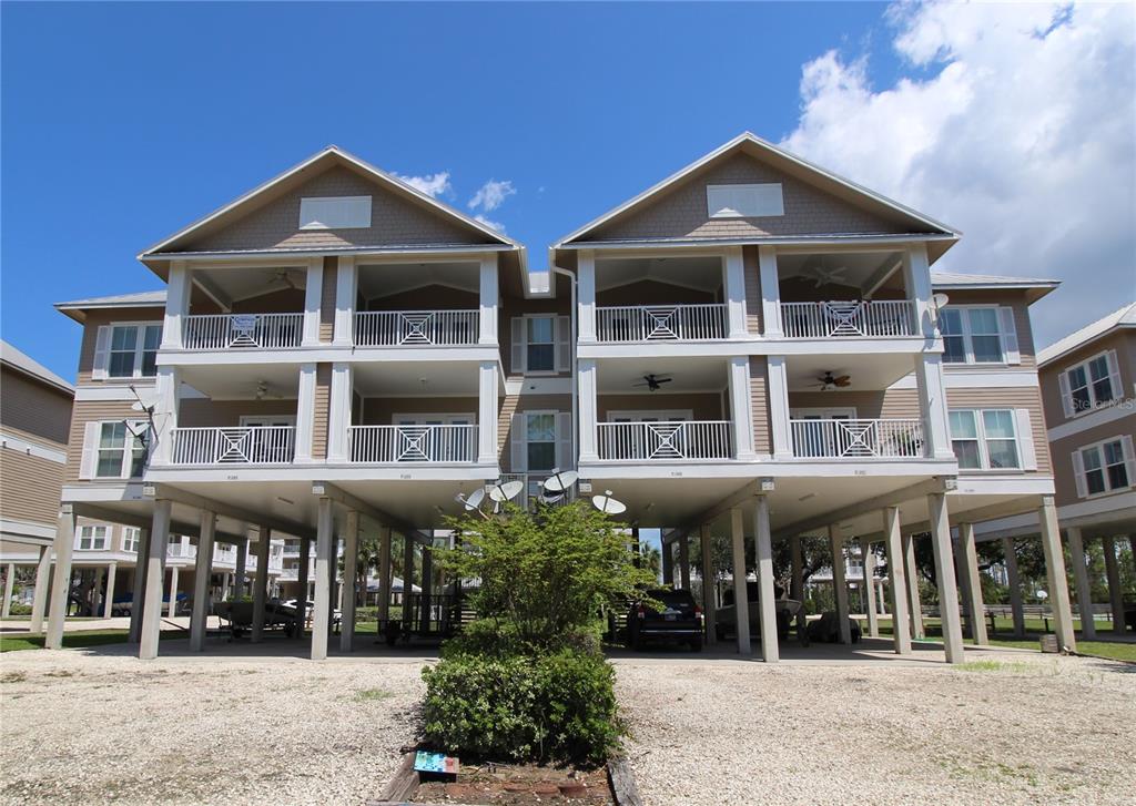 A three-story elevated residential building with balconies and a gravel parking area underneath — 221 3RD AVENUE E UNIT F-102, HORSESHOE BEACH, FL