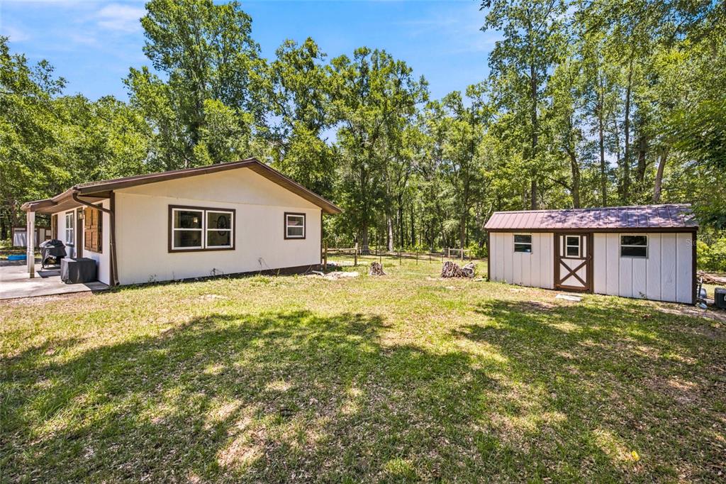 A single-story house and a detached shed sit on a grassy lot with surrounding trees — 13051 NE 60TH STREET, WILLISTON, FL