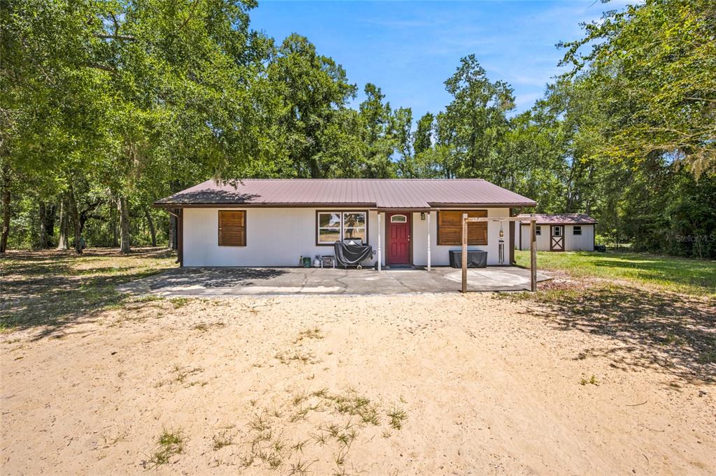 A single-story house with a metal roof, white siding, and a concrete patio area — 13051 NE 60TH STREET, WILLISTON, FL