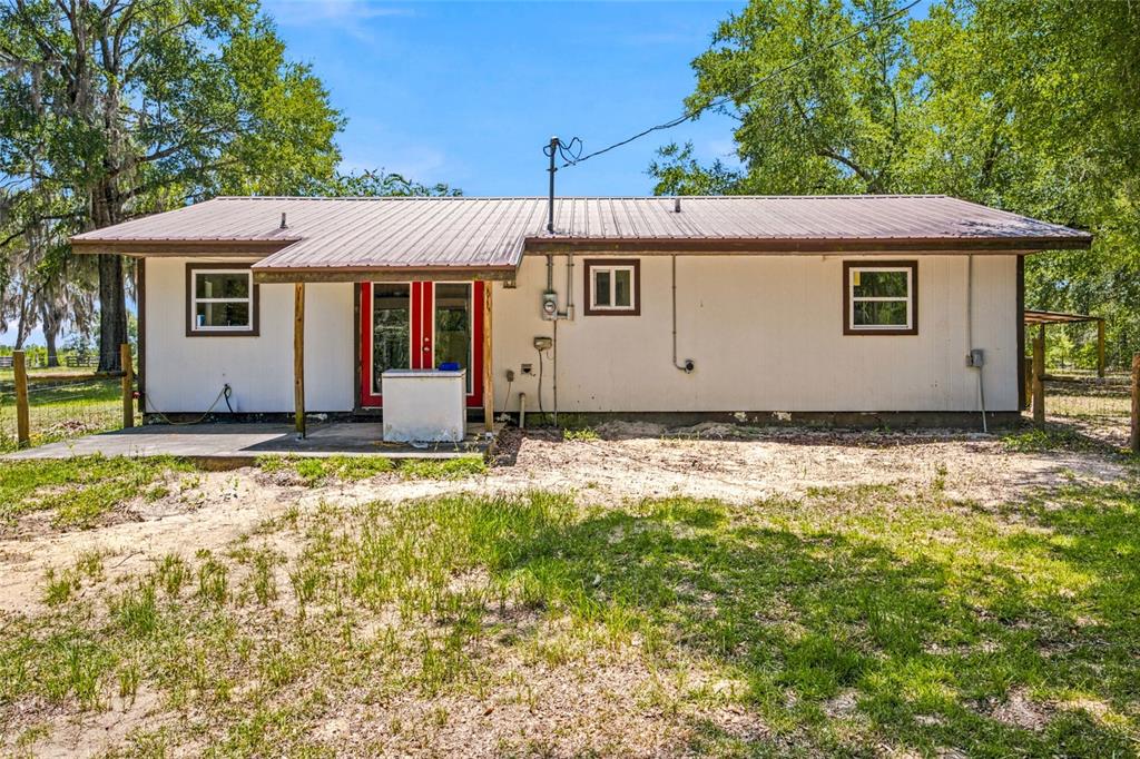 The exterior of a single-story house features white siding, a metal roof, and red doors — 13051 NE 60TH STREET, WILLISTON, FL