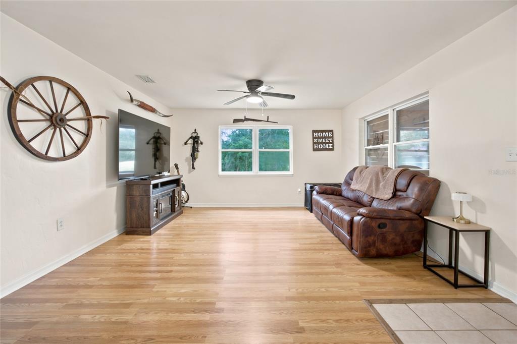 A living room features wood-look flooring, a brown leather sofa, and western-themed wall decor — 13051 NE 60TH STREET, WILLISTON, FL