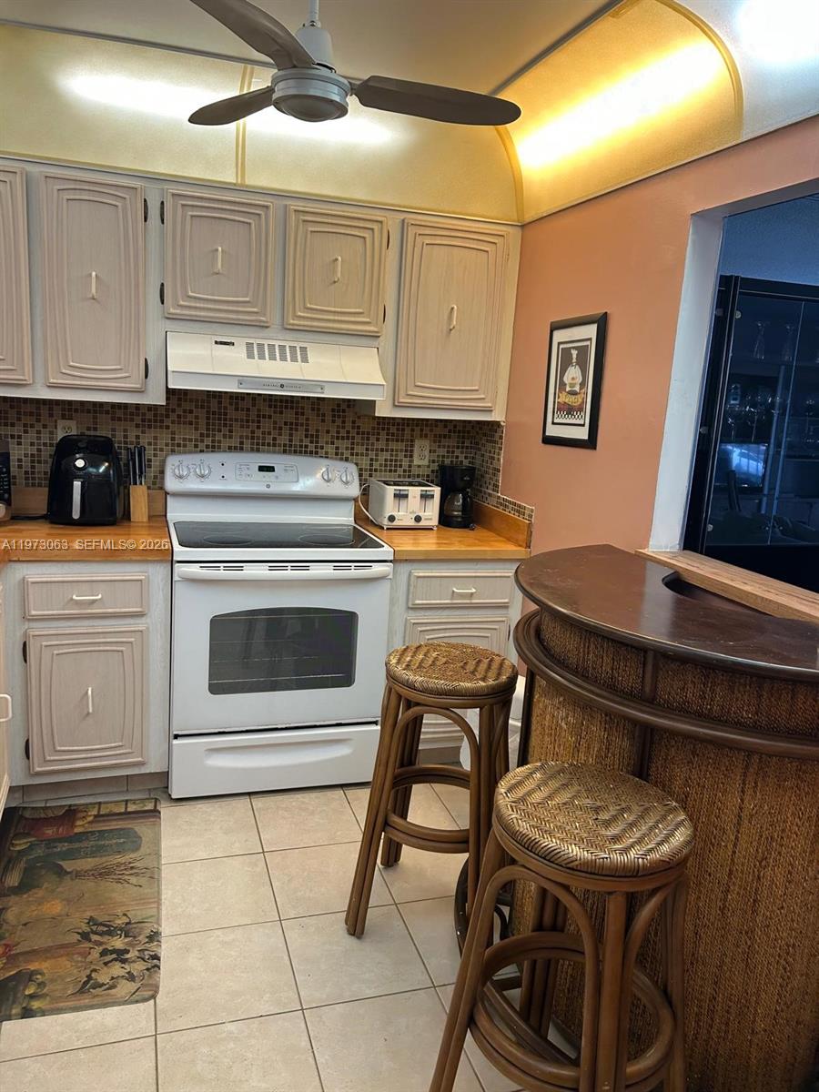 A kitchen features light-colored cabinets, a white stove, a breakfast bar, and two wicker stools — 3821 Environ Blvd # 202, Lauderhill FL 33319, LAUDERHILL, FL