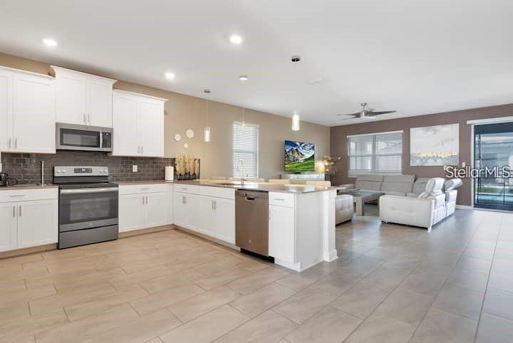 An open-concept kitchen with white cabinets and stainless steel appliances flows into a living area — 4535 NARRATIVE LANE, KISSIMMEE, FL