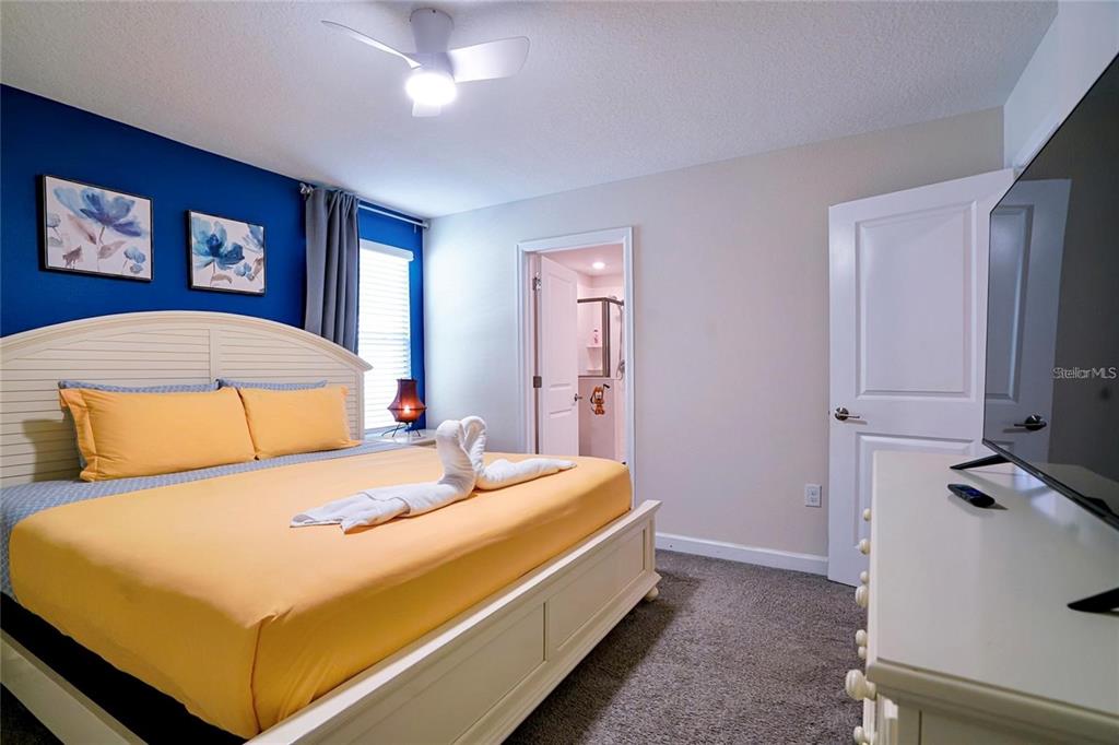 A bedroom features a bed with yellow bedding, a blue accent wall, and gray carpet — 4535 NARRATIVE LANE, KISSIMMEE, FL