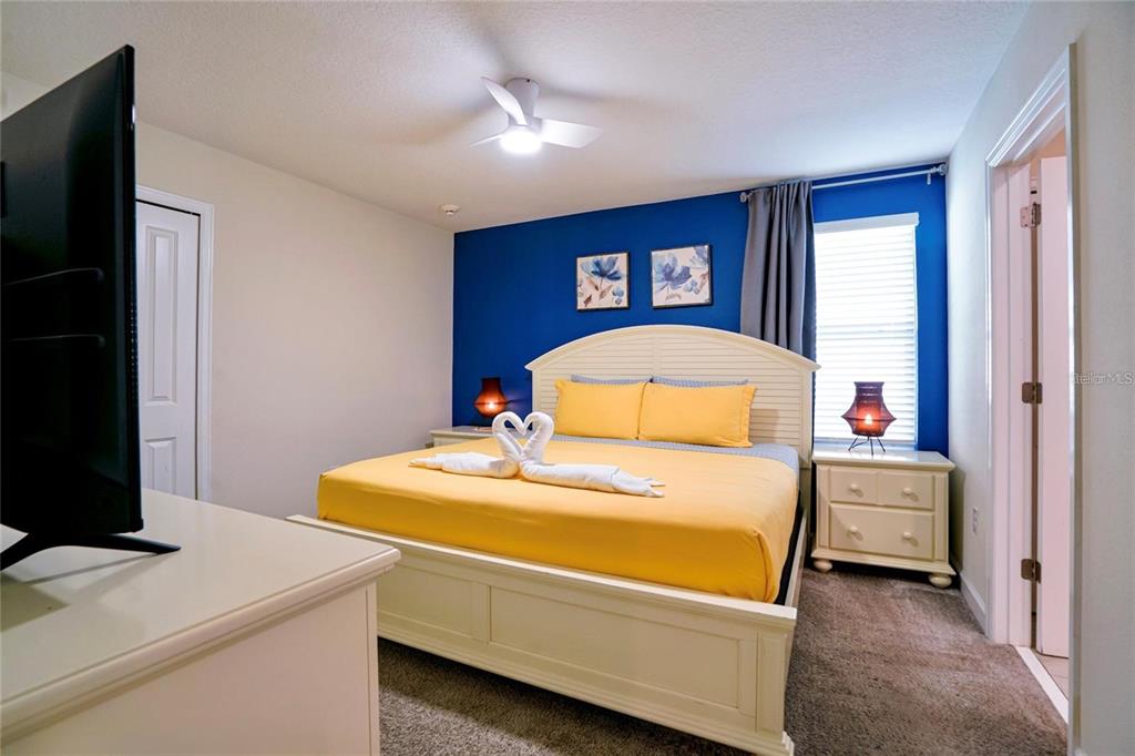 A bedroom features a bed with yellow linens, a blue accent wall, and white furniture — 4535 NARRATIVE LANE, KISSIMMEE, FL