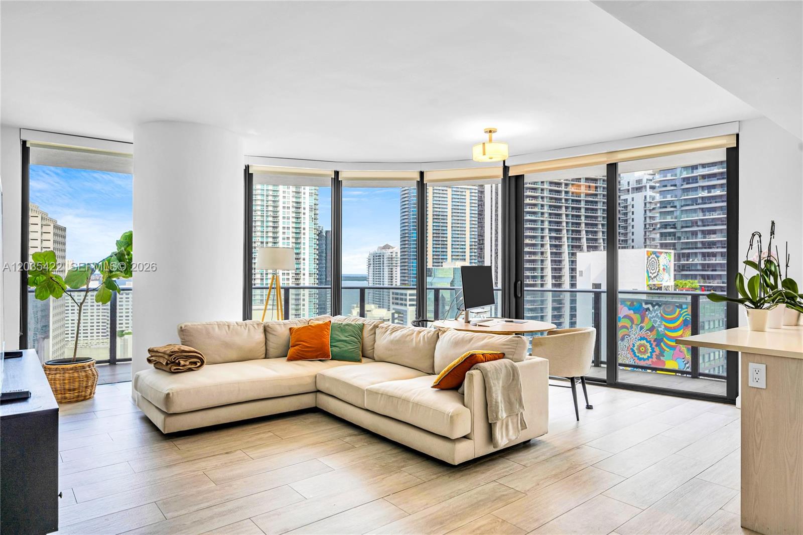 A living room features a beige sectional sofa, floor-to-ceiling windows, and views of city buildings — 45 SW 9th St # 2103, Miami FL 33130, MIAMI, FL