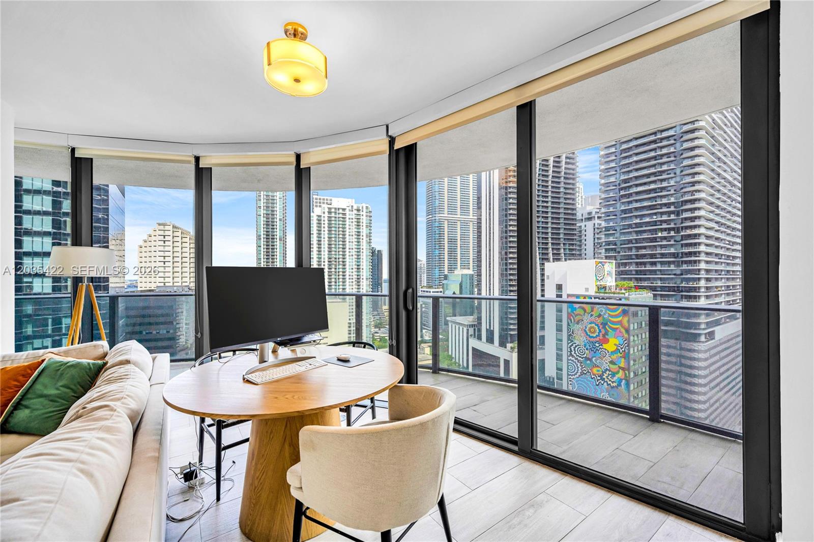 A room with a round wooden desk, computer, and floor-to-ceiling windows overlooking a city skyline — 45 SW 9th St # 2103, Miami FL 33130, MIAMI, FL