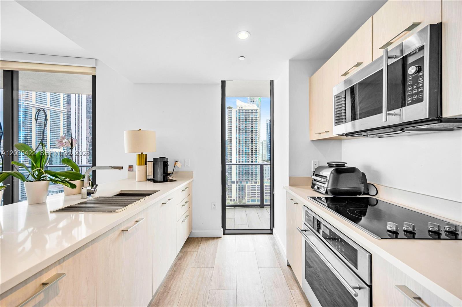 A modern galley kitchen features light wood cabinets, stainless steel appliances, and a balcony view — 45 SW 9th St # 2103, Miami FL 33130, MIAMI, FL