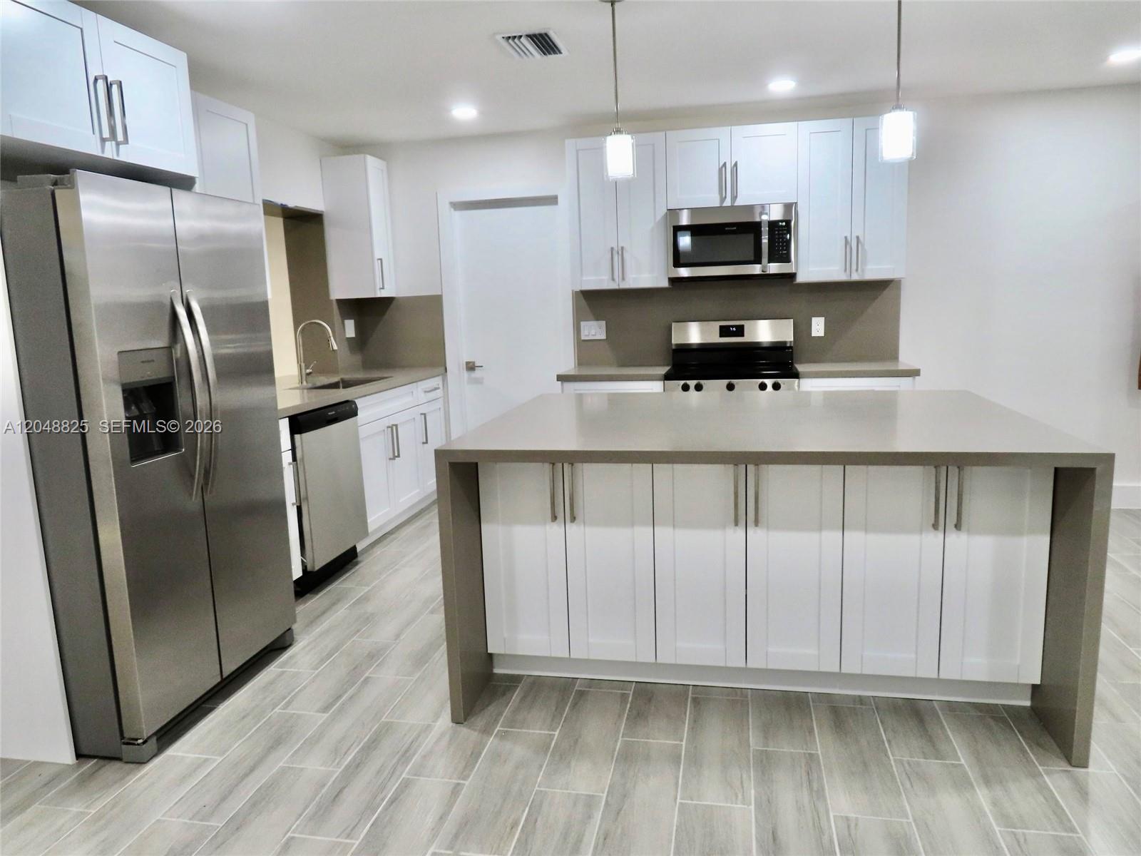 A modern kitchen features white cabinets, stainless steel appliances, and a large gray island — 1030 SW 96th Ave # 1030, Miami FL 33174, MIAMI, FL