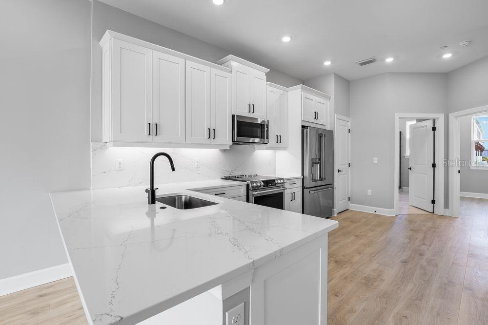 A modern kitchen features white cabinets, quartz countertops, stainless steel appliances, and light wood flooring — 1623 SEA HAVEN DRIVE UNIT 303, PUNTA GORDA, FL