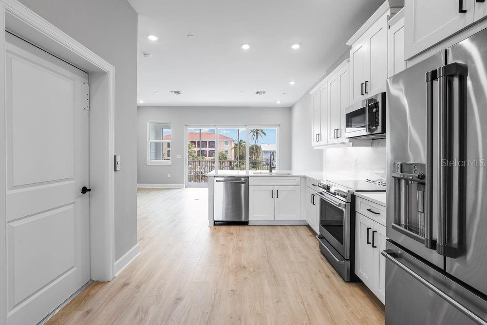 A modern kitchen with white cabinets, stainless steel appliances, and light wood-look flooring — 1623 SEA HAVEN DRIVE UNIT 303, PUNTA GORDA, FL