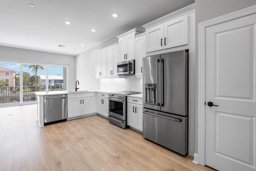 A modern kitchen features white cabinetry, stainless steel appliances, and light wood-look flooring — 1623 SEA HAVEN DRIVE UNIT 303, PUNTA GORDA, FL