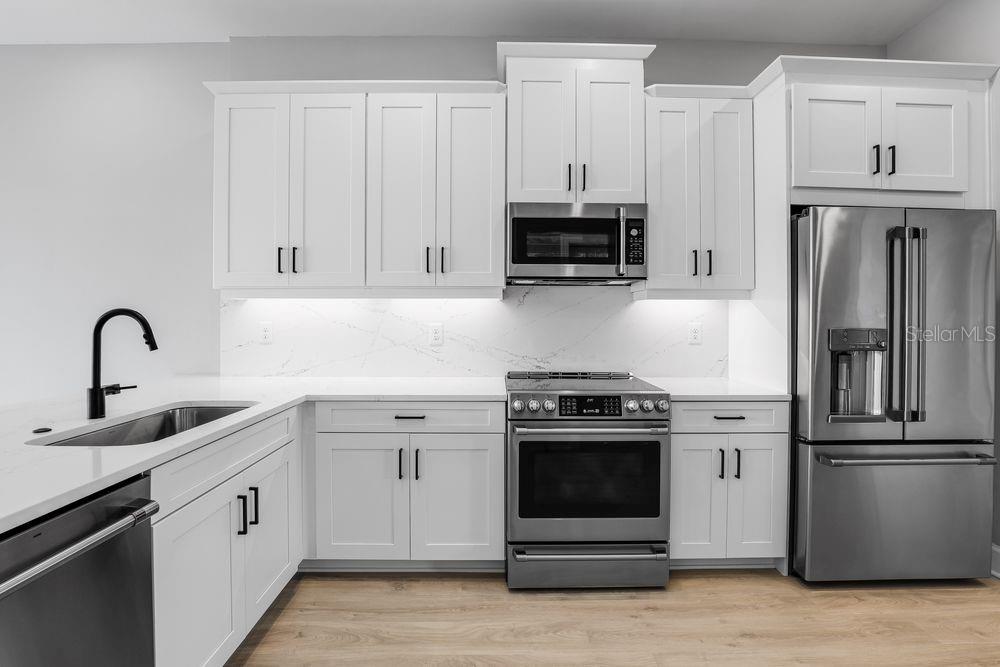A modern kitchen features white shaker cabinets, stainless steel appliances, and a marble-patterned backsplash — 1623 SEA HAVEN DRIVE UNIT 303, PUNTA GORDA, FL