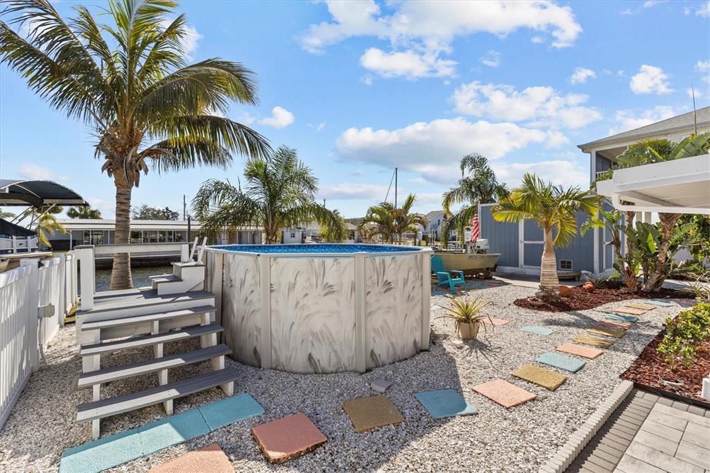 An above-ground pool sits in a gravel backyard with colorful stepping stones and palm trees — 13604 MARIA DRIVE, HUDSON, FL