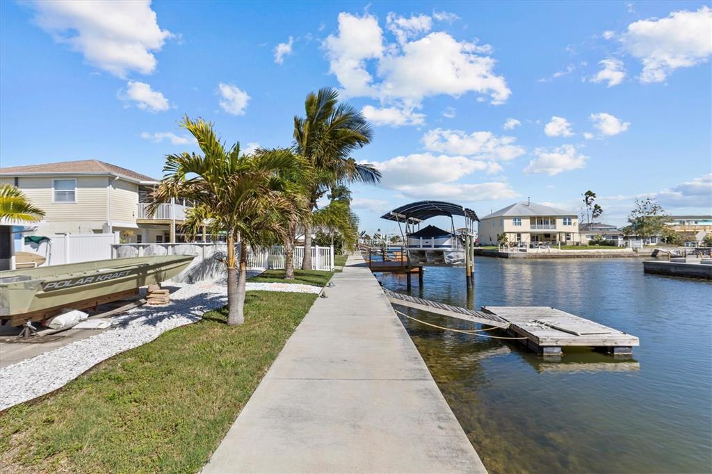 A concrete walkway runs along a canal next to a house and a boat lift — 13604 MARIA DRIVE, HUDSON, FL