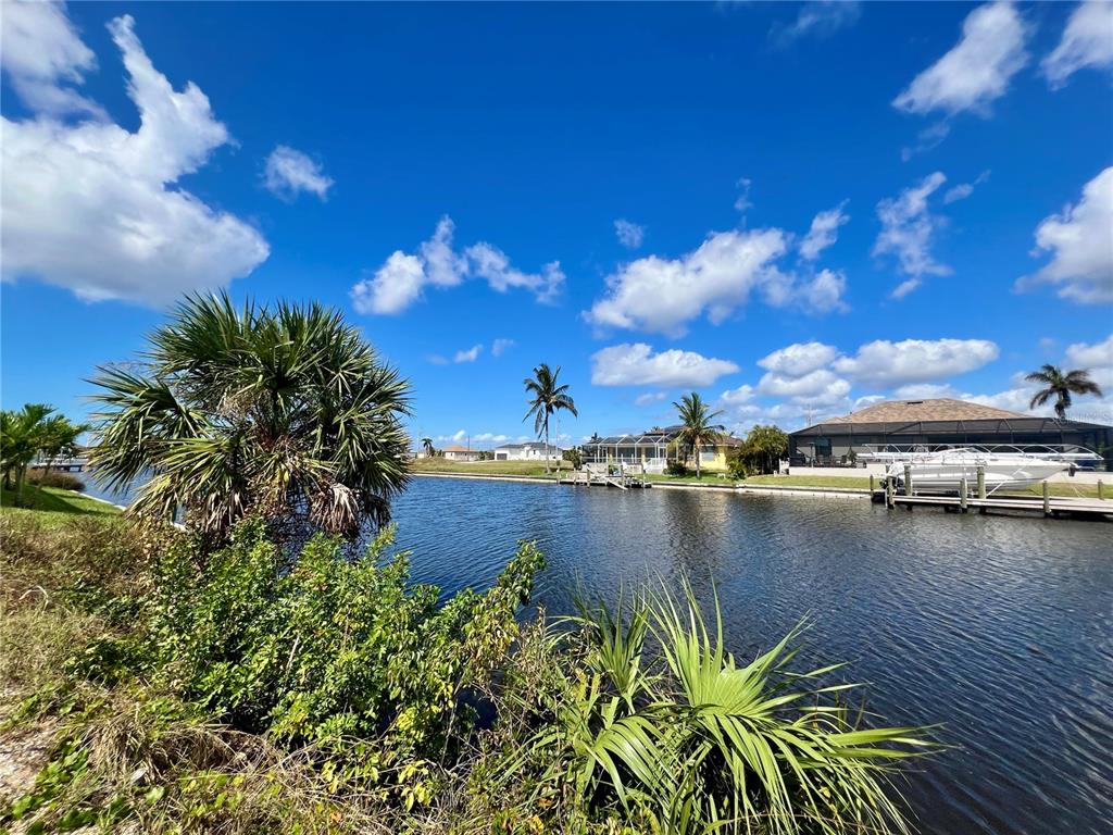 A canal view featuring palm trees, a boat dock, and residential homes under a blue sky — 4109 NW 36TH TERRACE, CAPE CORAL, FL