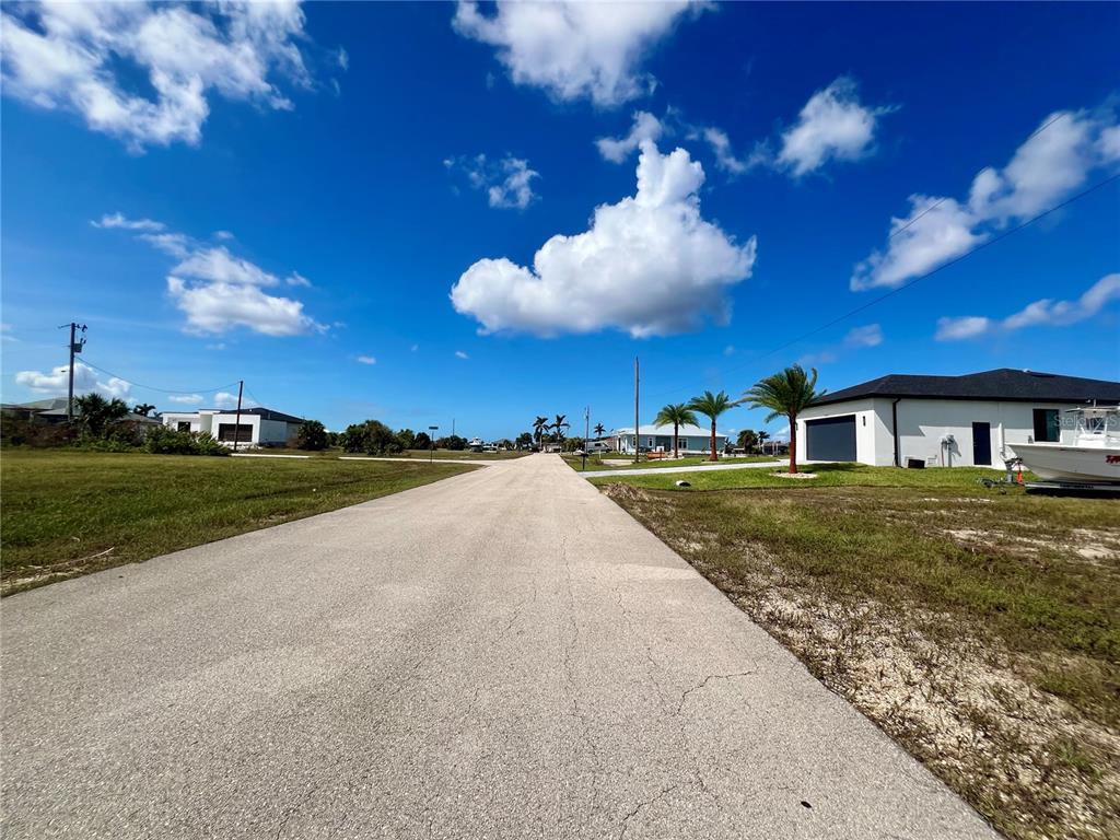 A paved road leads through a residential neighborhood with houses and palm trees under a sky — 4109 NW 36TH TERRACE, CAPE CORAL, FL