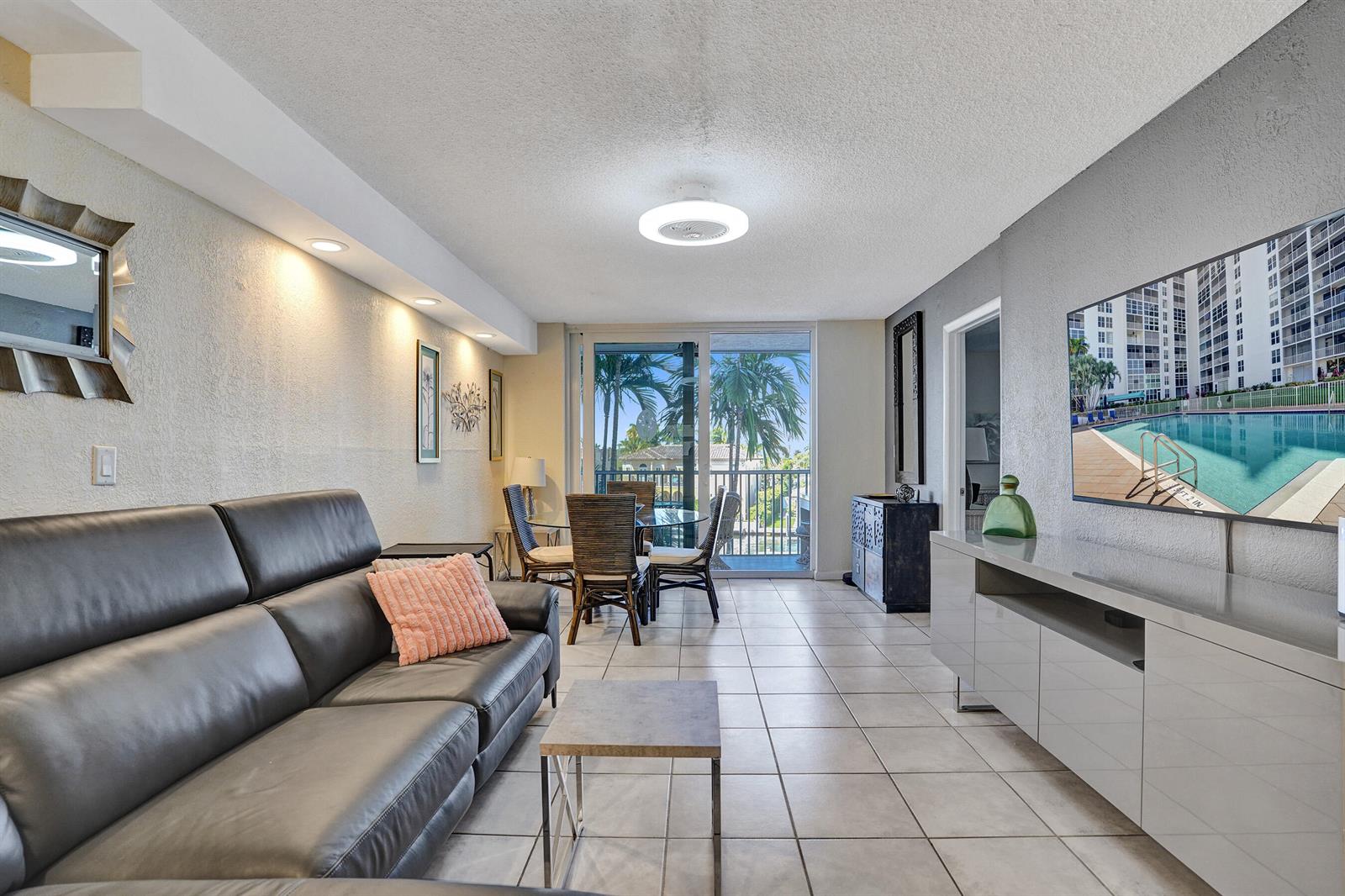 A living room with a dark leather sofa, tile floors, and a dining area overlooking a balcony — 1391 S Ocean Boulevard, Pompano Beach FL 33062, POMPANO BEACH, FL