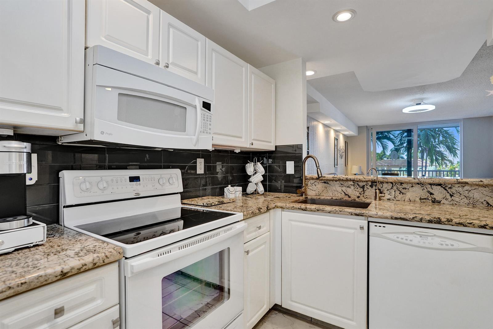 A kitchen features white cabinetry, granite countertops, a black tile backsplash, and white appliances — 1391 S Ocean Boulevard, Pompano Beach FL 33062, POMPANO BEACH, FL