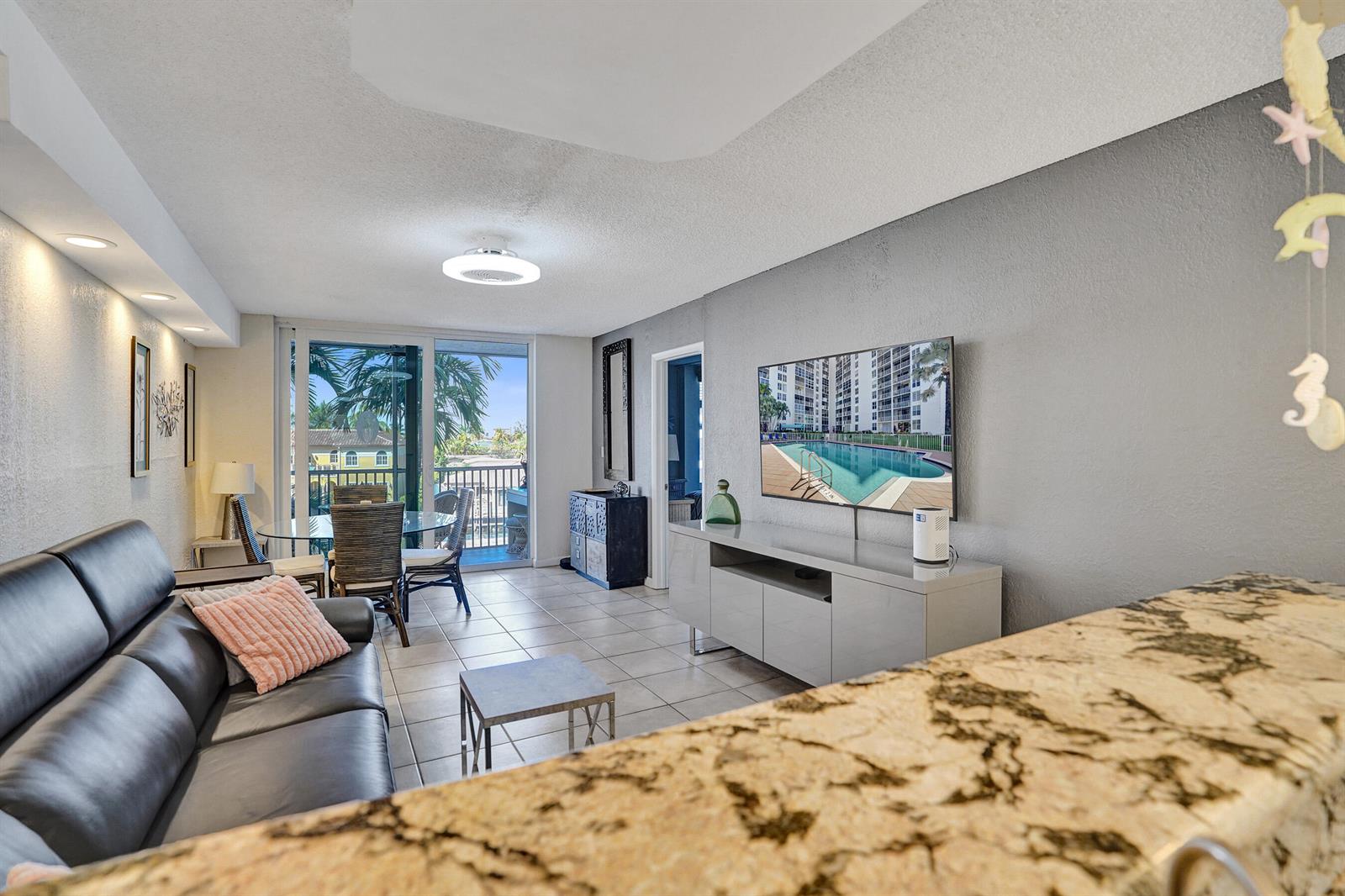 A living room features a black leather sofa, a television, and a balcony view — 1391 S Ocean Boulevard, Pompano Beach FL 33062, POMPANO BEACH, FL