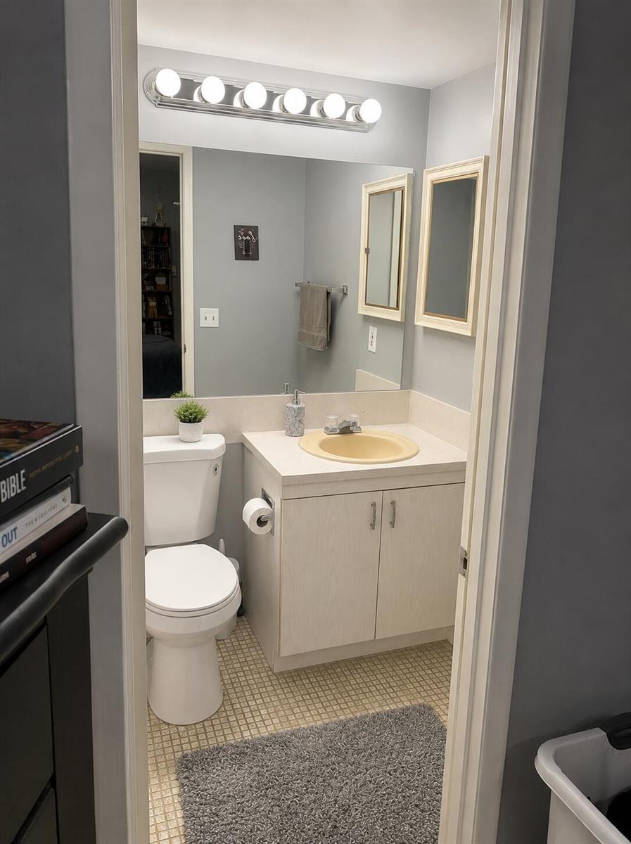 A small bathroom features a light-colored vanity with a yellow sink, toilet, and wall mirror — 2013 Lincoln A, Boca Raton FL 33434, BOCA RATON, FL