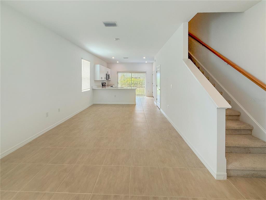 An open-concept living area features tile flooring, a kitchen with white cabinets, and carpeted stairs — 8948 DAYBREAK STREET, SARASOTA, FL