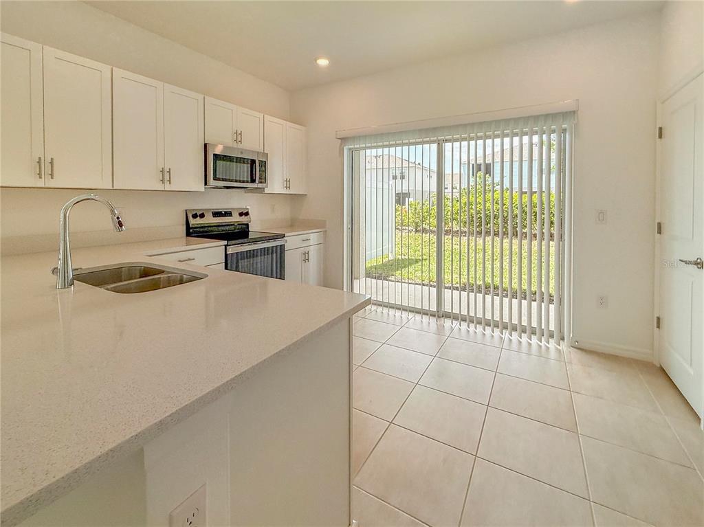 A kitchen with white cabinets, stainless steel appliances, and a sliding glass door to outside — 8948 DAYBREAK STREET, SARASOTA, FL
