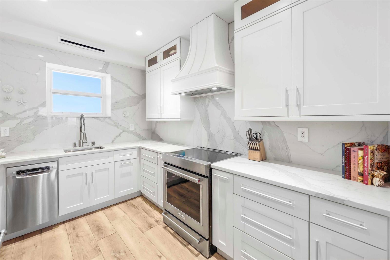 A modern kitchen features white cabinets, marble-style countertops, stainless steel appliances, and wood-look flooring — 2921 S Ocean Boulevard # 704, Highland Beach FL 33487, HIGHLAND BEACH, FL