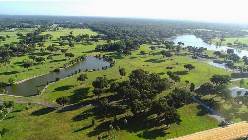 An aerial view shows a large grassy landscape with scattered trees, ponds, and paved paths — 16070 SE 55 AVE RD, SUMMERFIELD, FL